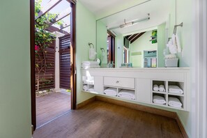 A bathroom with a large mirror, white vanity, multiple towel racks, and a wooden floor.