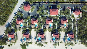 Vista aérea de un complejo turístico frente a la playa con varias construcciones tipo bungalow, cada una con techo rojo y piscina.