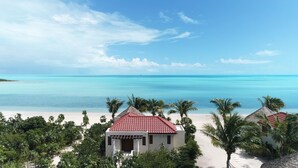Blick auf einen Strand mit blauem Himmel, türkisblauem Wasser und einem Weg zu einem Gebäude mit rotem Dach.