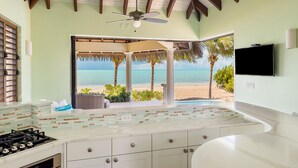 Eine Küche mit Blick auf den Strand, einem Deckenventilator und einem an der Wand befestigten Fernseher.