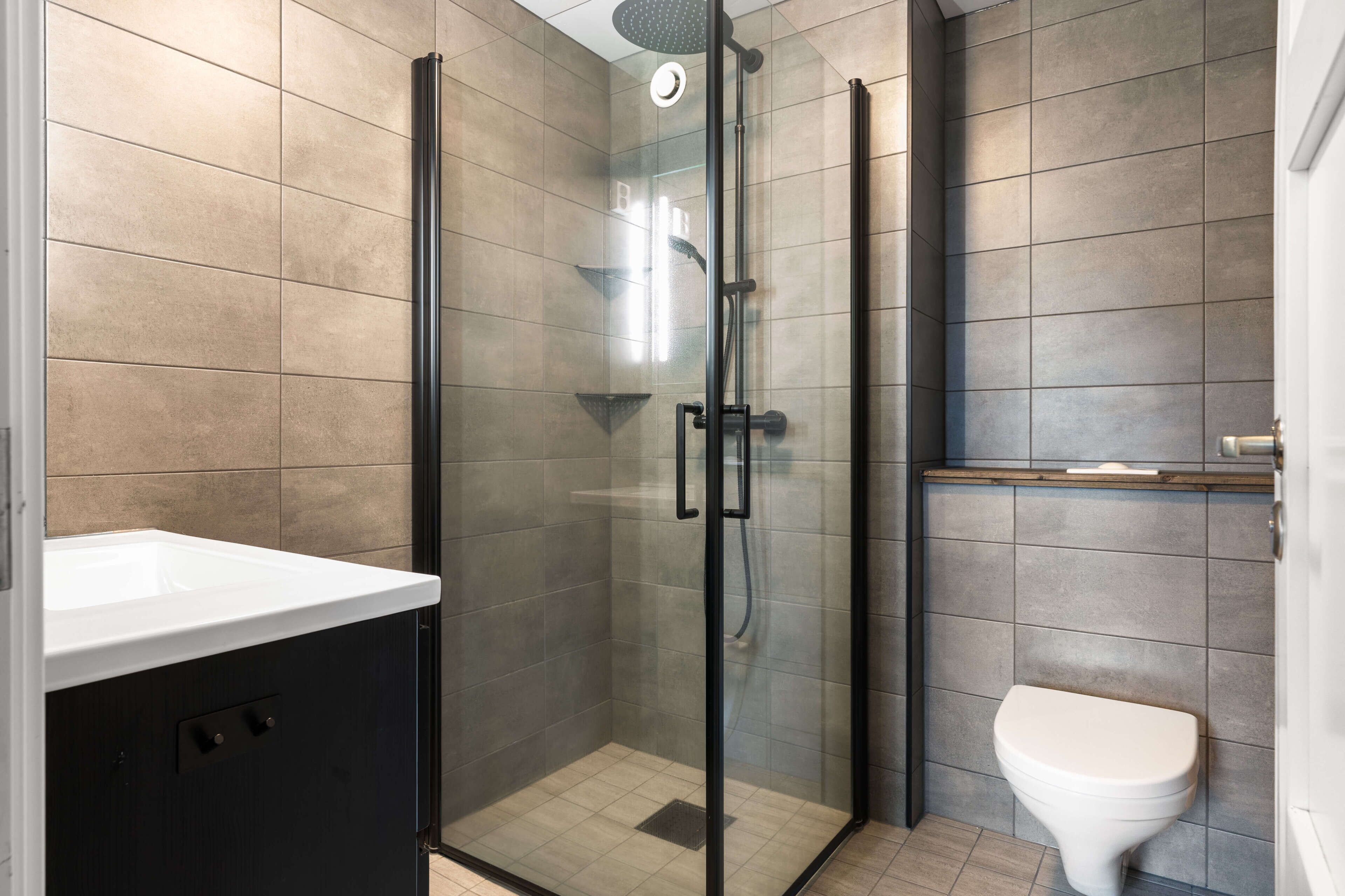 Un bagno moderno con doccia a vetro, un water bianco e un mobile contenitore nero.