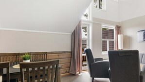 A room with a dining table, chairs, a grey sofa, a potted plant, and a window with curtains. - Trysilfjell Apartment Hotel (Trysil)