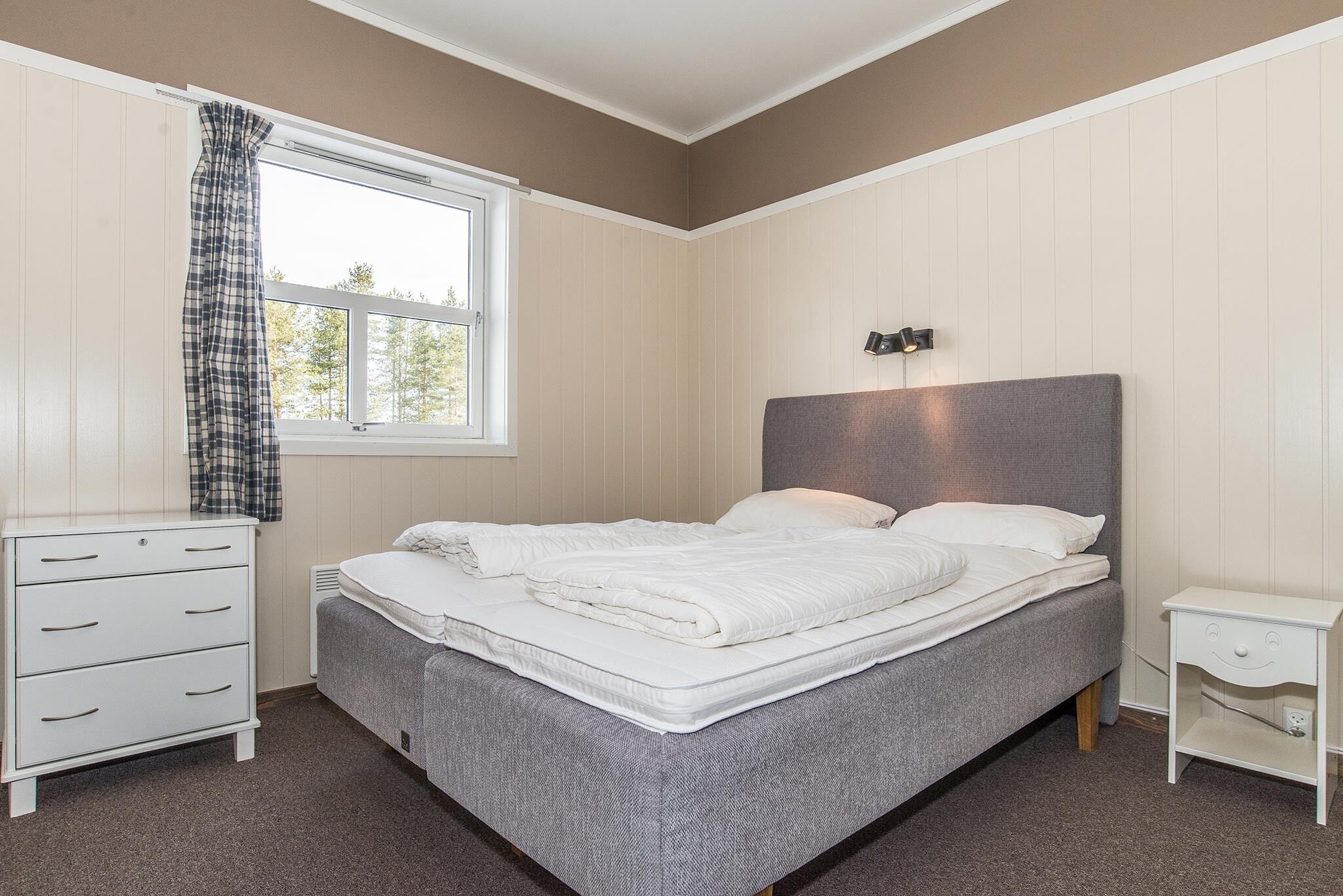 A bedroom with a bed, a dresser, a nightstand, and a window with curtains.