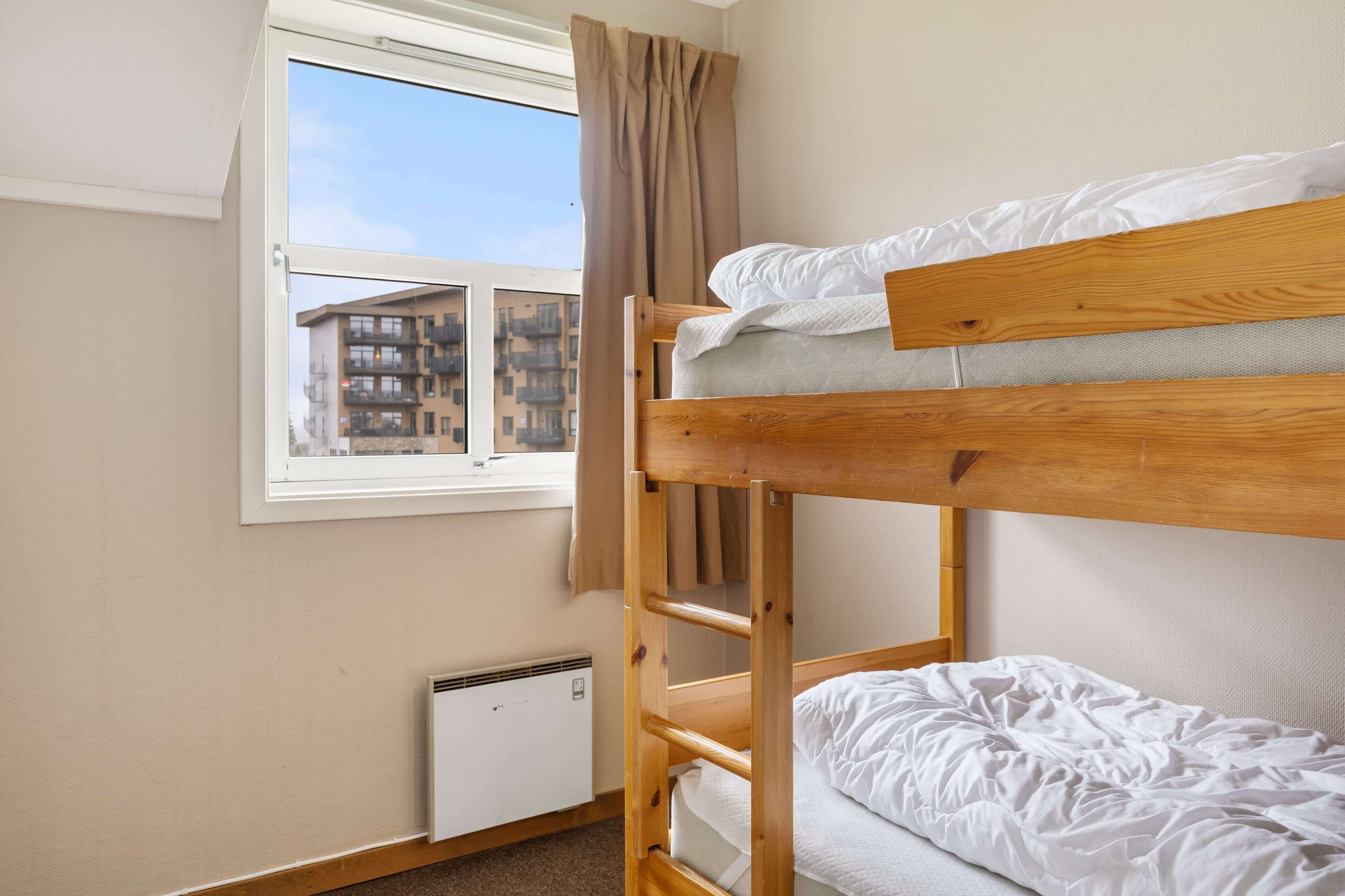 Dormitorio con literas, ventana, radiador y vista a edificios.
