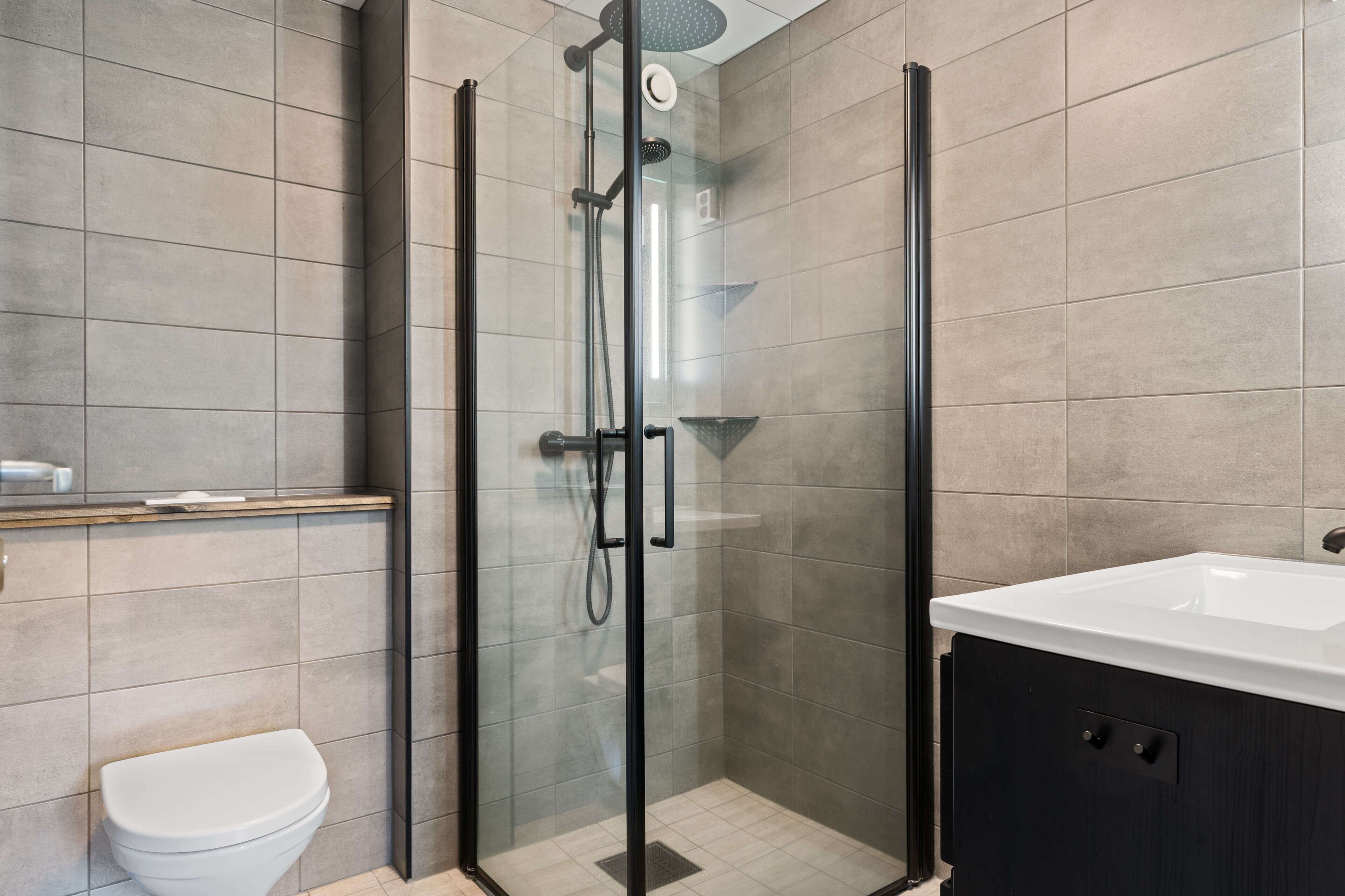 A modern bathroom with a glass-enclosed shower, a white toilet, and a dark cabinet with a white sink.