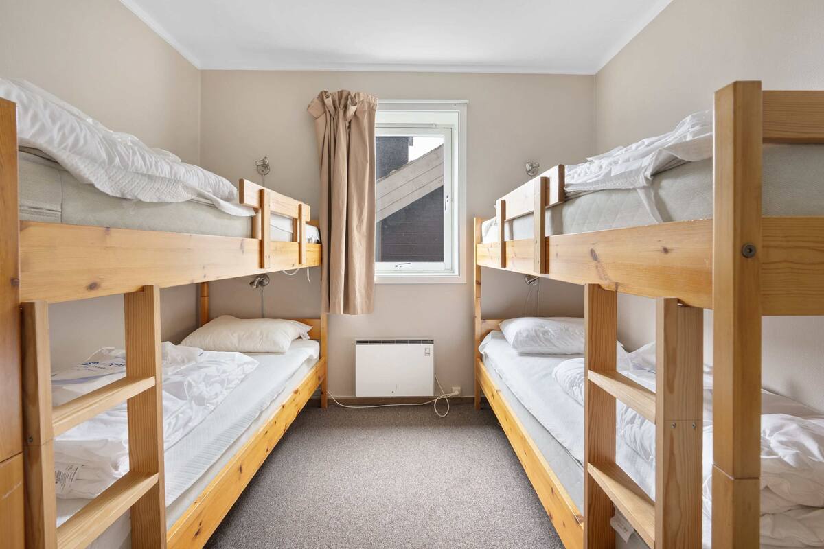 A dormitory room with bunk beds, a window with curtains, and a radiator.