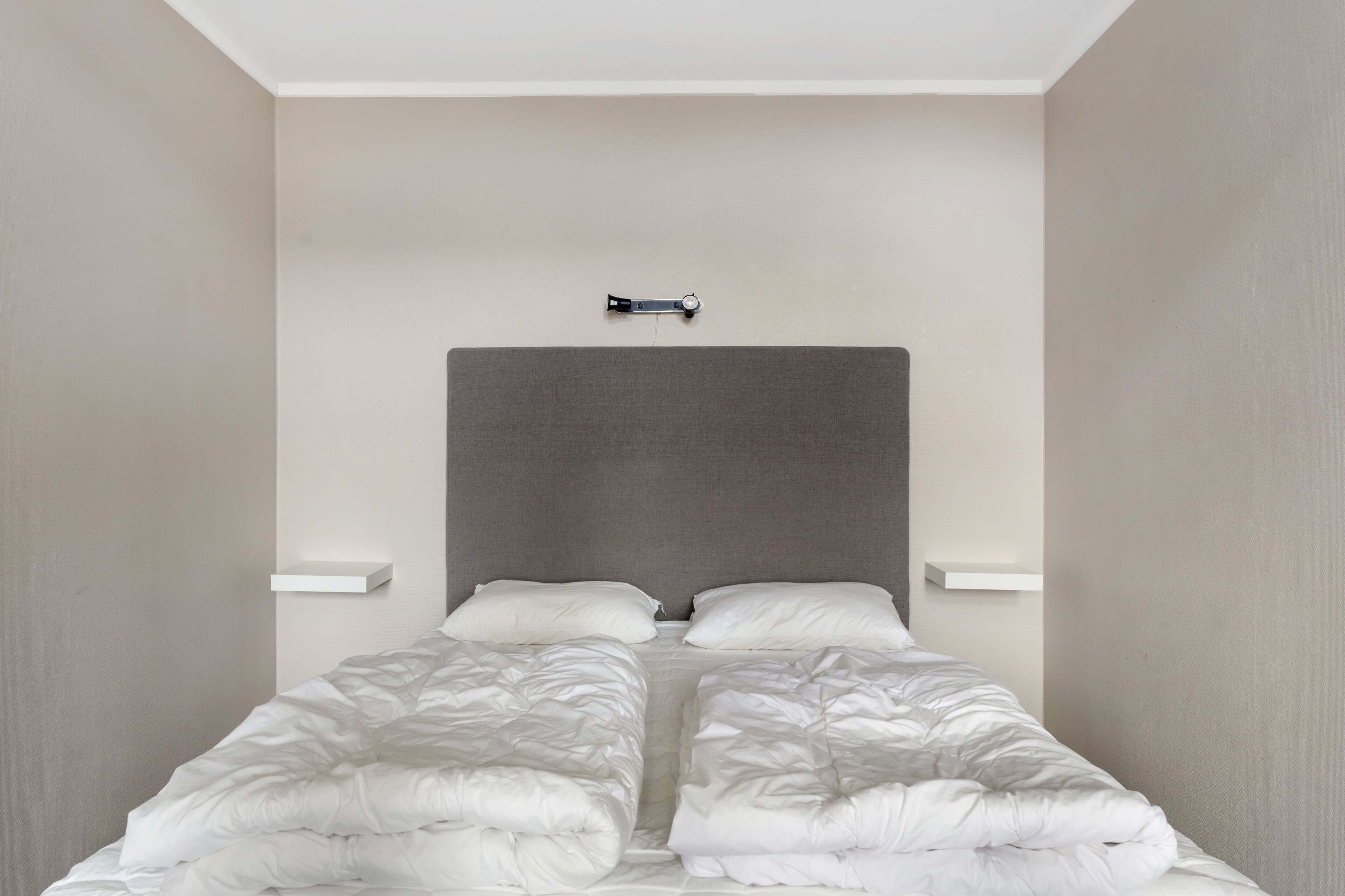 Una cama con cabecera gris, dos almohadas blancas y edredón blanco.
