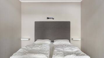 Una cama con cabecera gris, dos almohadas blancas y edredón blanco.