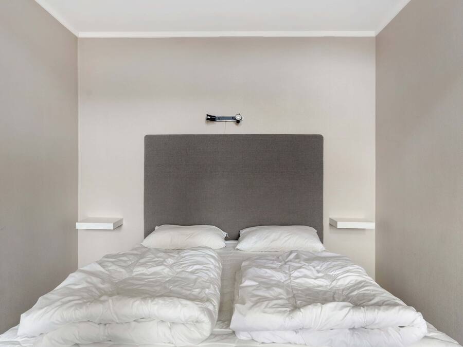 Una cama con cabecera gris, dos almohadas blancas y edredón blanco.