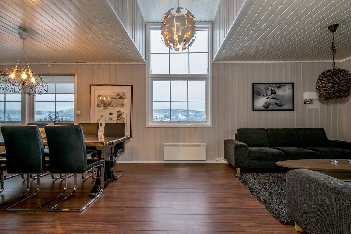 A modern living room with a dining area, large windows, and a view of the outdoors.