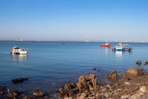A coastal scene with boats on calm water, rocky shoreline, and distant buildings.