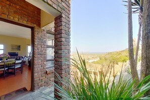 A room with a brick wall, a dining area with a table and chairs, and a view of a distant landscape.