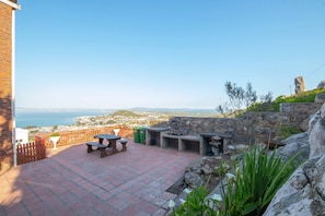 A patio with outdoor seating, a stone wall, and a view of the sea.