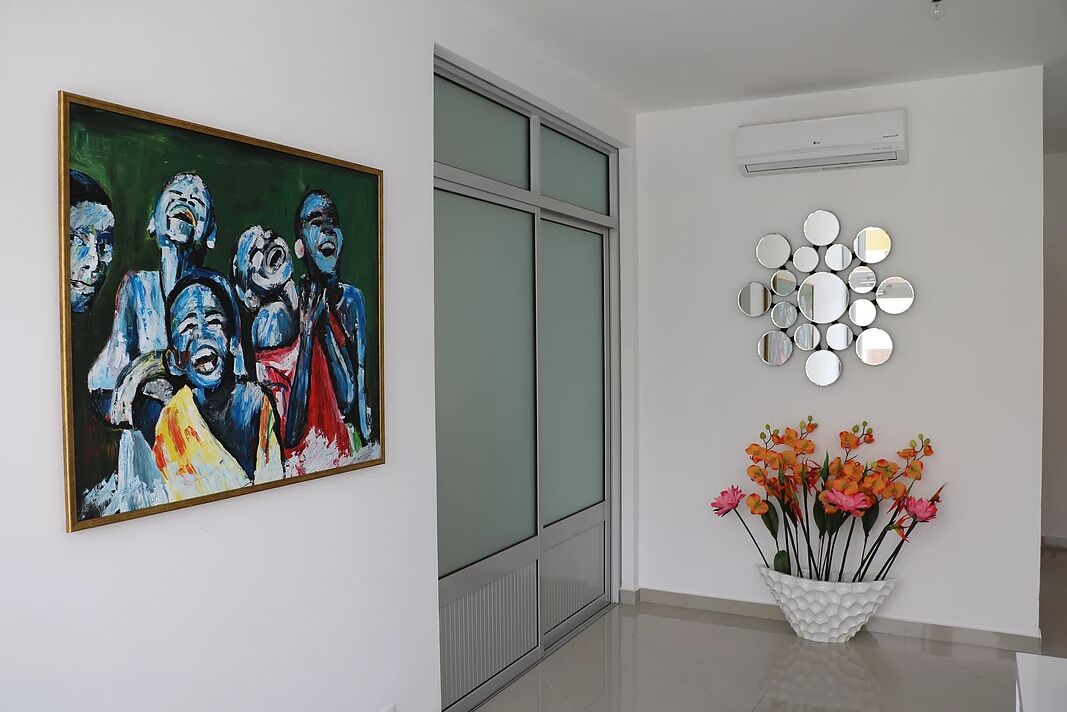 A room with a large abstract painting, a wall-mounted mirror arrangement, and a vase with flowers.