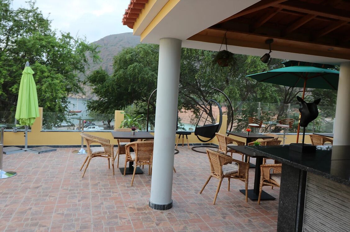An outdoor patio with wicker furniture and a green umbrella, overlooking a mountainous landscape.