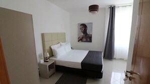 Un dormitorio con cama, mesita de noche, lámpara, un cuadro en la pared y una puerta.