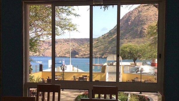 Habitación con un amplio ventanal con vistas a la costa, barcos y un paisaje montañoso.