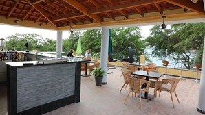 Un patio al aire libre con barra, muebles de mimbre y vista al agua.