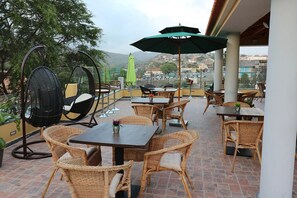 Een terras buiten met wicker meubels, een tafel met een groene parasol, en een uitzicht op de skyline op de achtergrond.