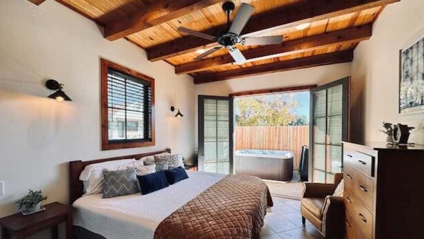 Een slaapkamer met een bed, houten plafond, plafondventilator, dressoir en uitzicht.