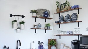 Een keuken met een zwarte spoelbak, houten planken met keukengerei en hangende planten.