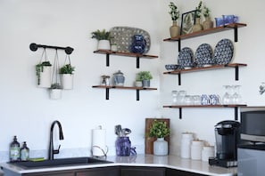 A kitchen with a black sink, wooden shelves with various kitchenware, and hanging plants.