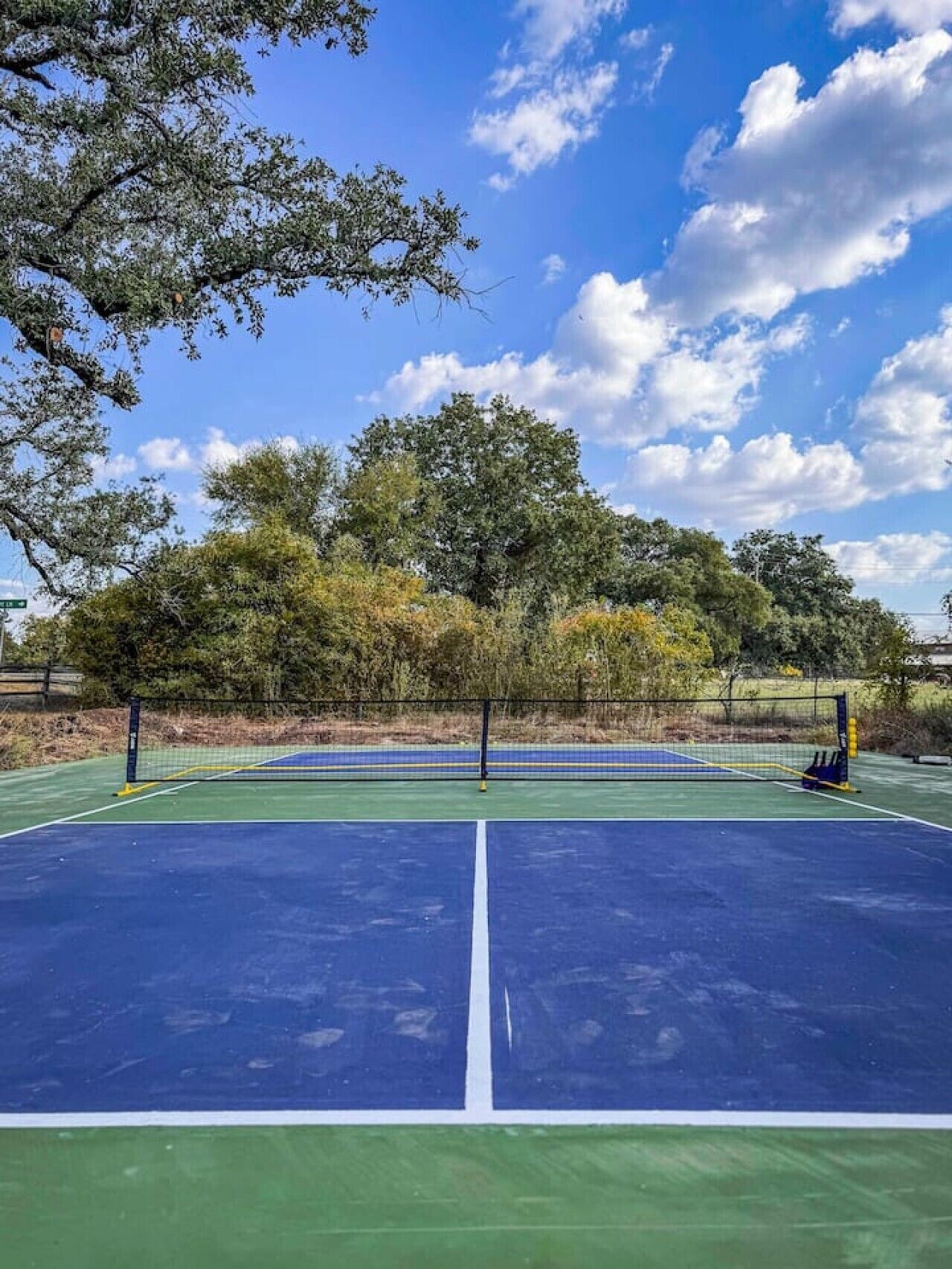Een tennisbaan buiten met een net, omgeven door bomen en een heldere lucht.