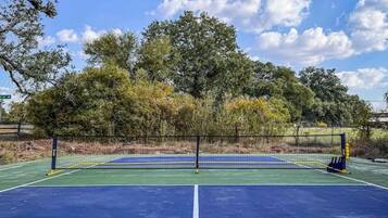 Een tennisbaan buiten met een net, omgeven door bomen en een heldere lucht.