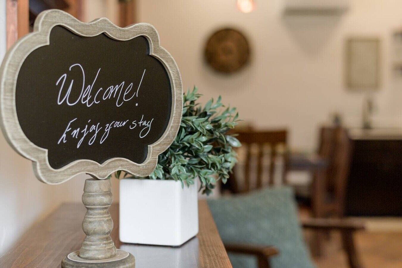 A welcome sign with a rustic design, placed on a wooden table with a potted plant beside it.