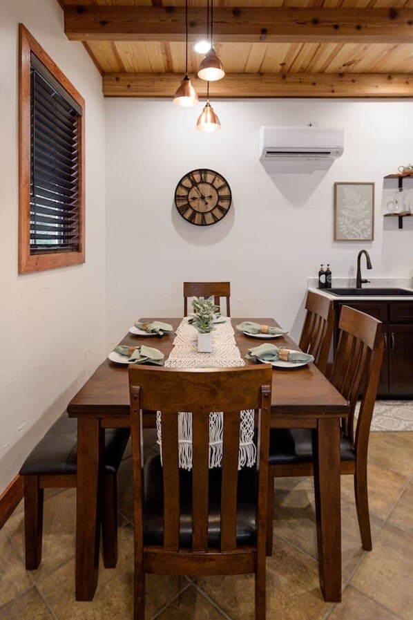 A dining area with a wooden table, chairs, a clock, and pendant lights.