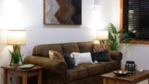 A brown leather sofa with cushions, two wooden side tables with lamps, a decorative plate, and a small plant. - Little Dutch Cabin #100 | Soaker Tub | Pickleball (Waco)