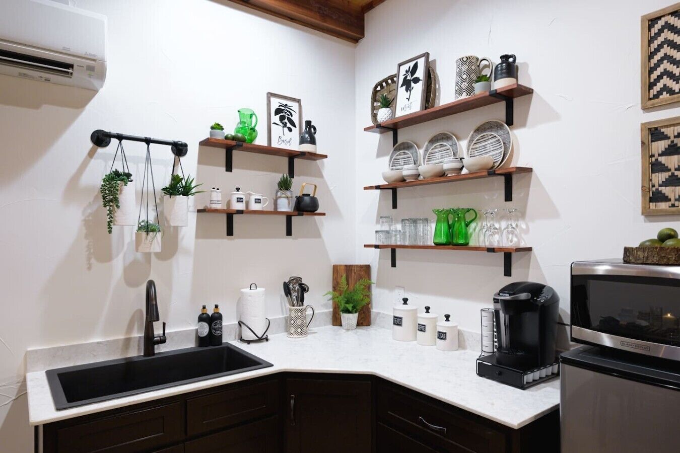 Una cocina con un lavamanos negro, encimera blanca y estantes con utensilios de cocina.