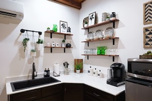 A kitchen with a black sink, white countertop, and shelves with kitchenware.