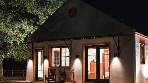 A building with large windows, a porch with chairs, and a door. - Little Dutch Cabin #100 | Soaker Tub | Pickleball (Waco)