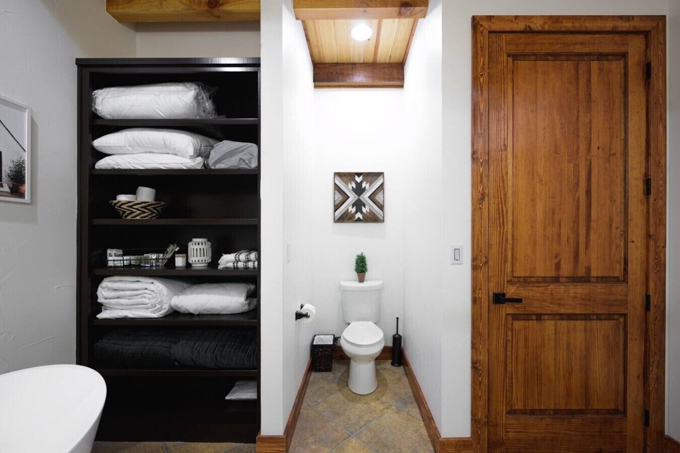 A bathroom with a toilet, a shelf with towels, a small plant, and a wooden door.