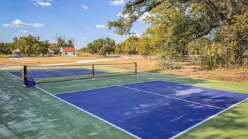 An outdoor tennis court with a net, surrounded by trees and a building in the background.