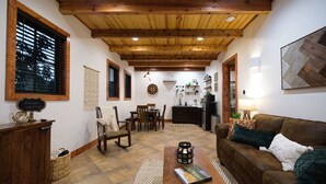 A cozy living room with a wooden ceiling, a fireplace, a dining area, and a kitchen in the background. - Little Dutch Cabin #100 | Soaker Tub | Pickleball (Waco)
