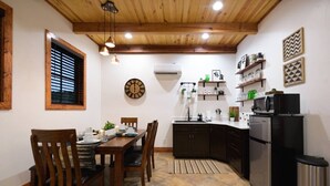 A compact kitchen with dark cabinets, a black refrigerator, and a microwave on top. There is a dining table with chairs and a clock on the wall. - Little Dutch Cabin #100 | Soaker Tub | Pickleball (Waco)