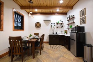 A compact kitchen with dark cabinets, a black refrigerator, and a microwave on top. There is a dining table with chairs and a clock on the wall. - Little Dutch Cabin #100 | Soaker Tub | Pickleball (Waco)