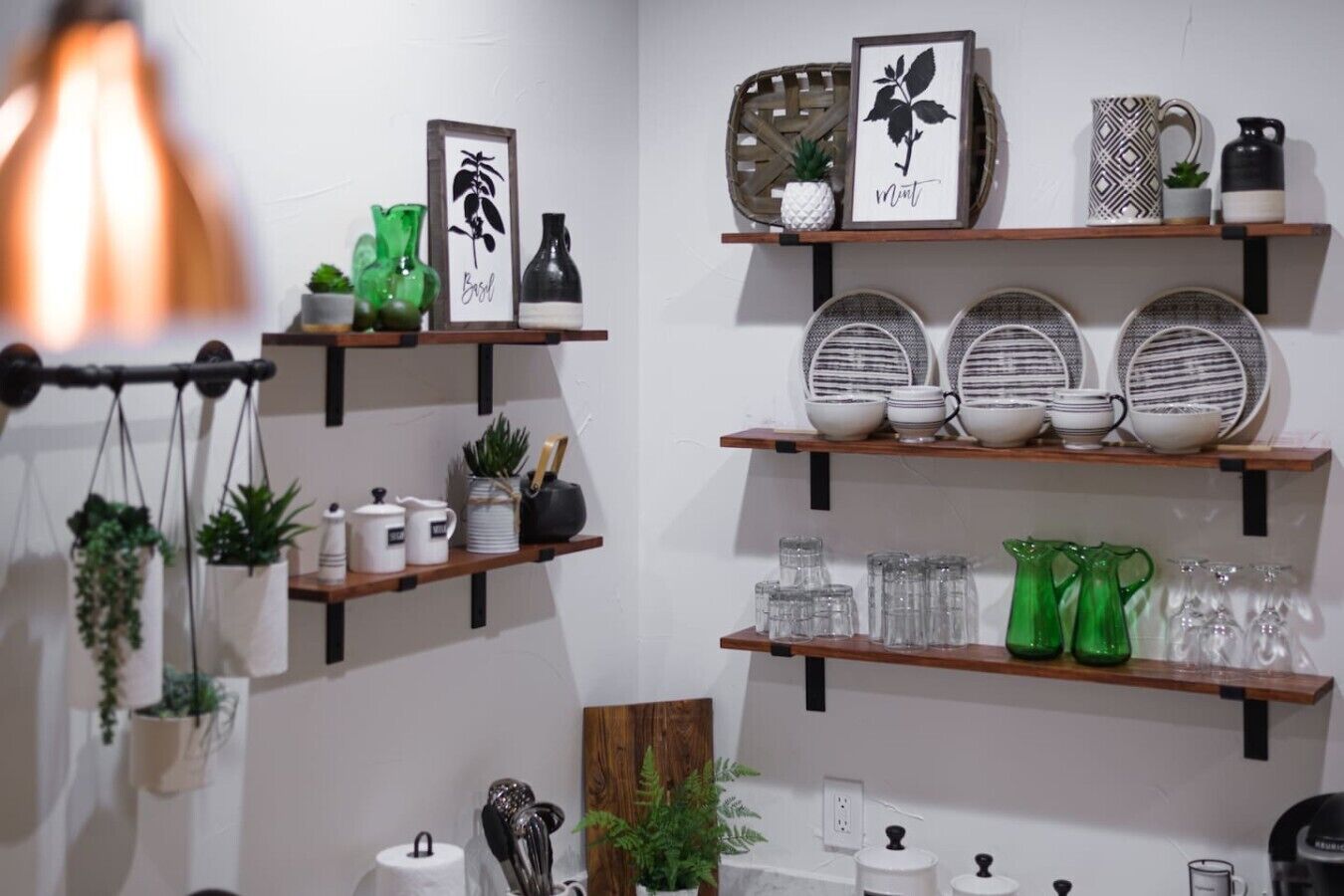 Een keuken met planken vol keukengerei, een hangplant en een botanische lithografie in een lijst.