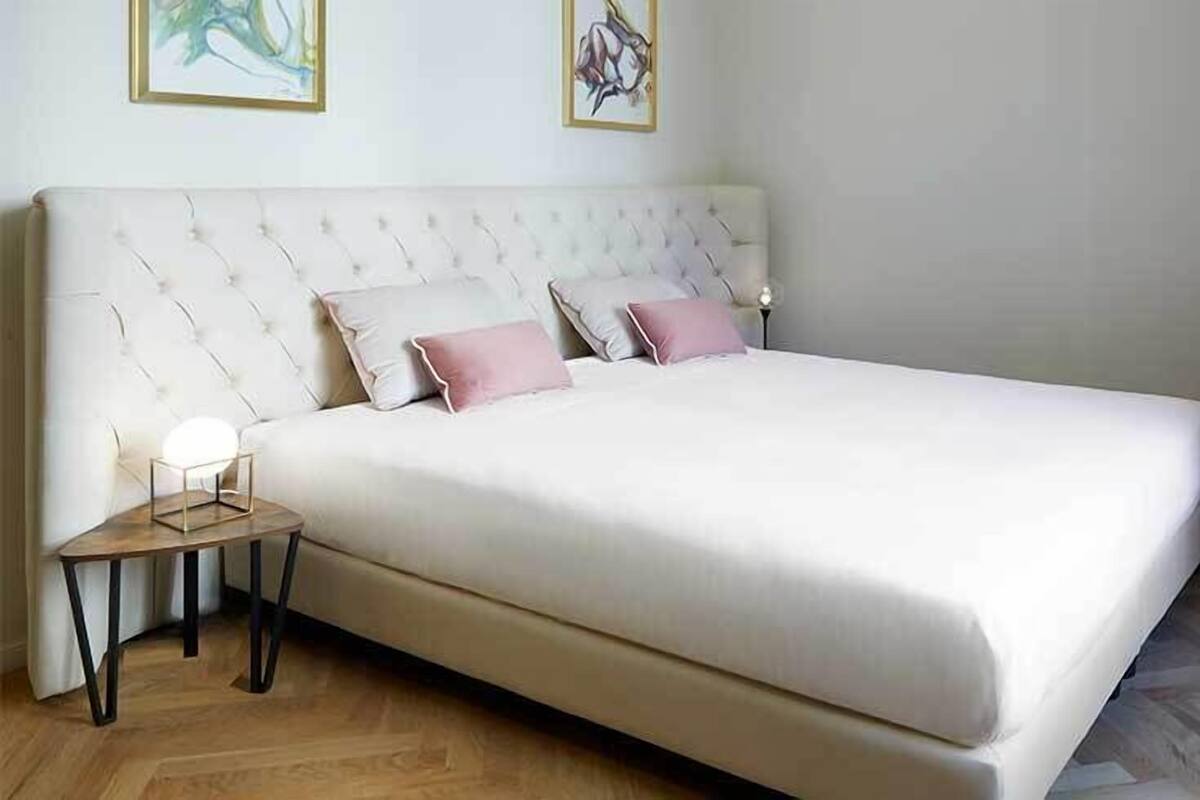 A neatly made bed with a tufted headboard, a bedside table with a lamp, and artwork on the wall.
