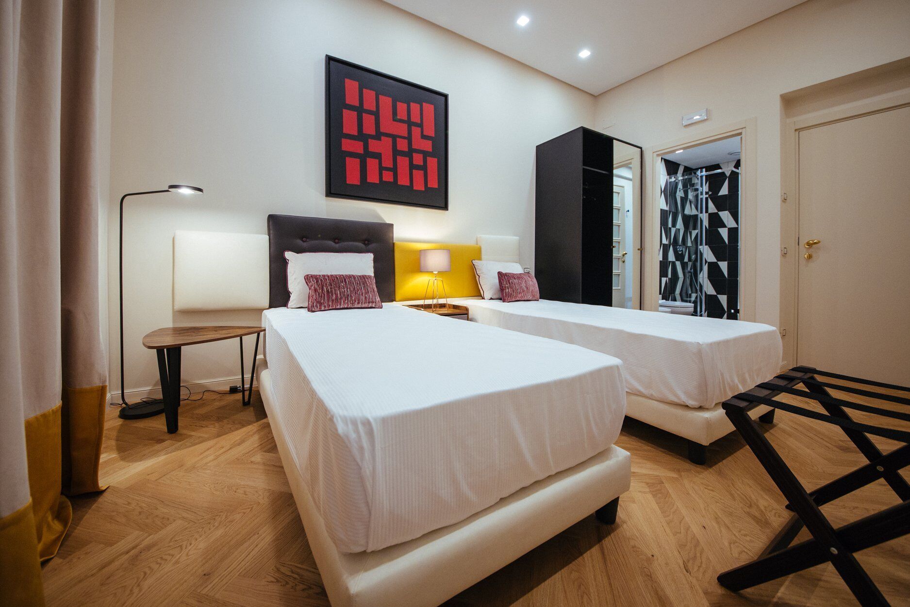 A hotel room with two beds, a desk, a lamp, and a large abstract artwork on the wall.