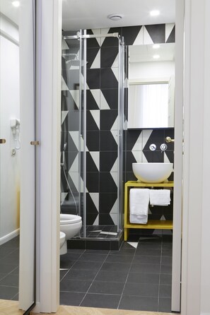 A modern bathroom with a black and white geometric tile backsplash, a glass-enclosed shower, a white sink, and a yellow vanity.