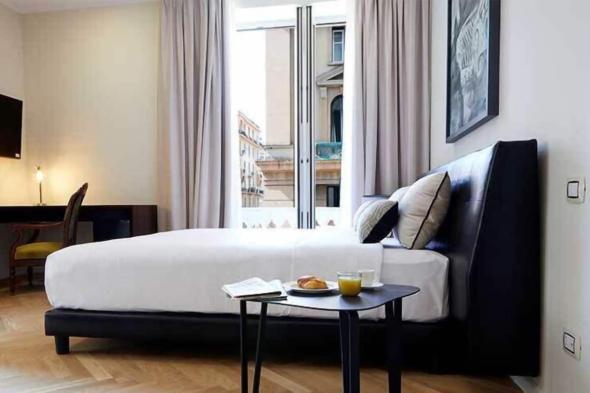 A hotel room with a bed, a desk, a chair, a small table with breakfast, and a TV on the wall.