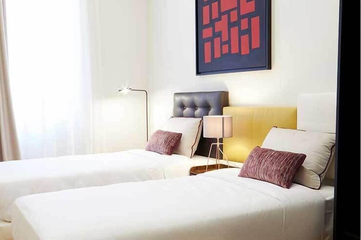 A hotel room with two beds, a modern lamp, and a geometric artwork on the wall.