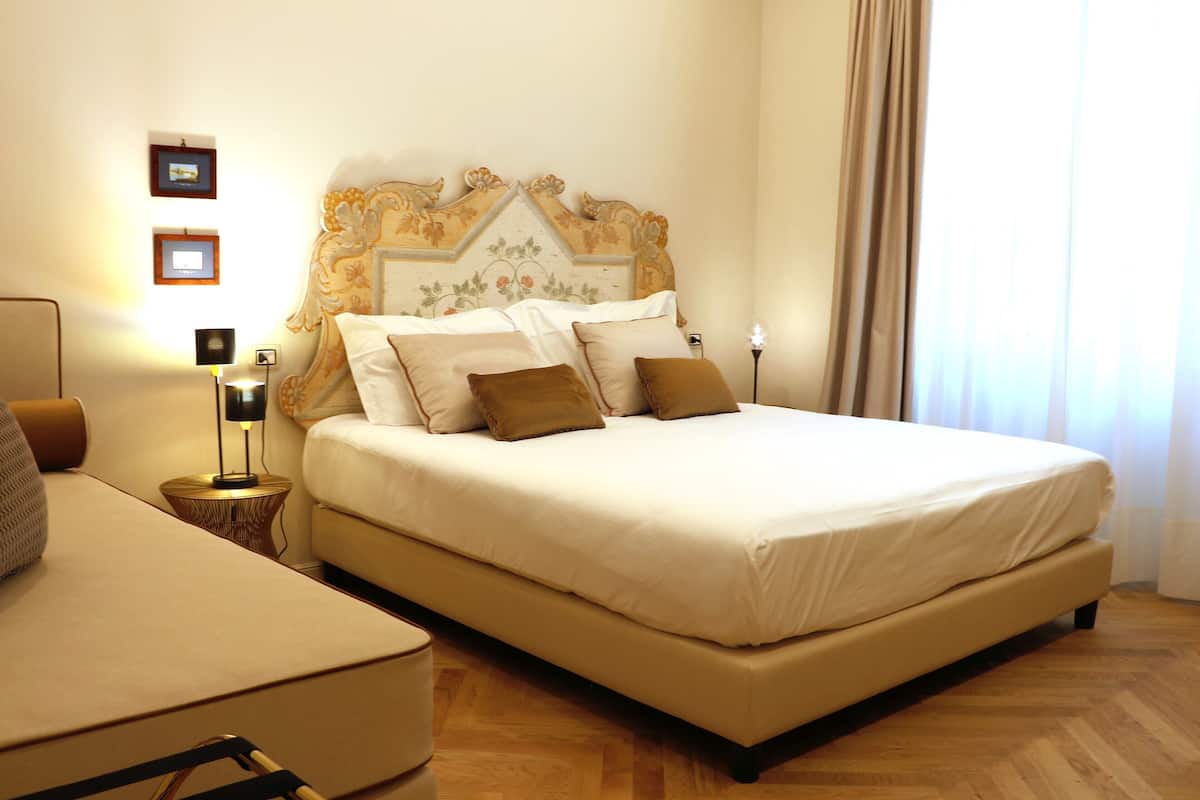 A bedroom with a large bed, a bedside table with a lamp, and a wall-mounted picture frame.