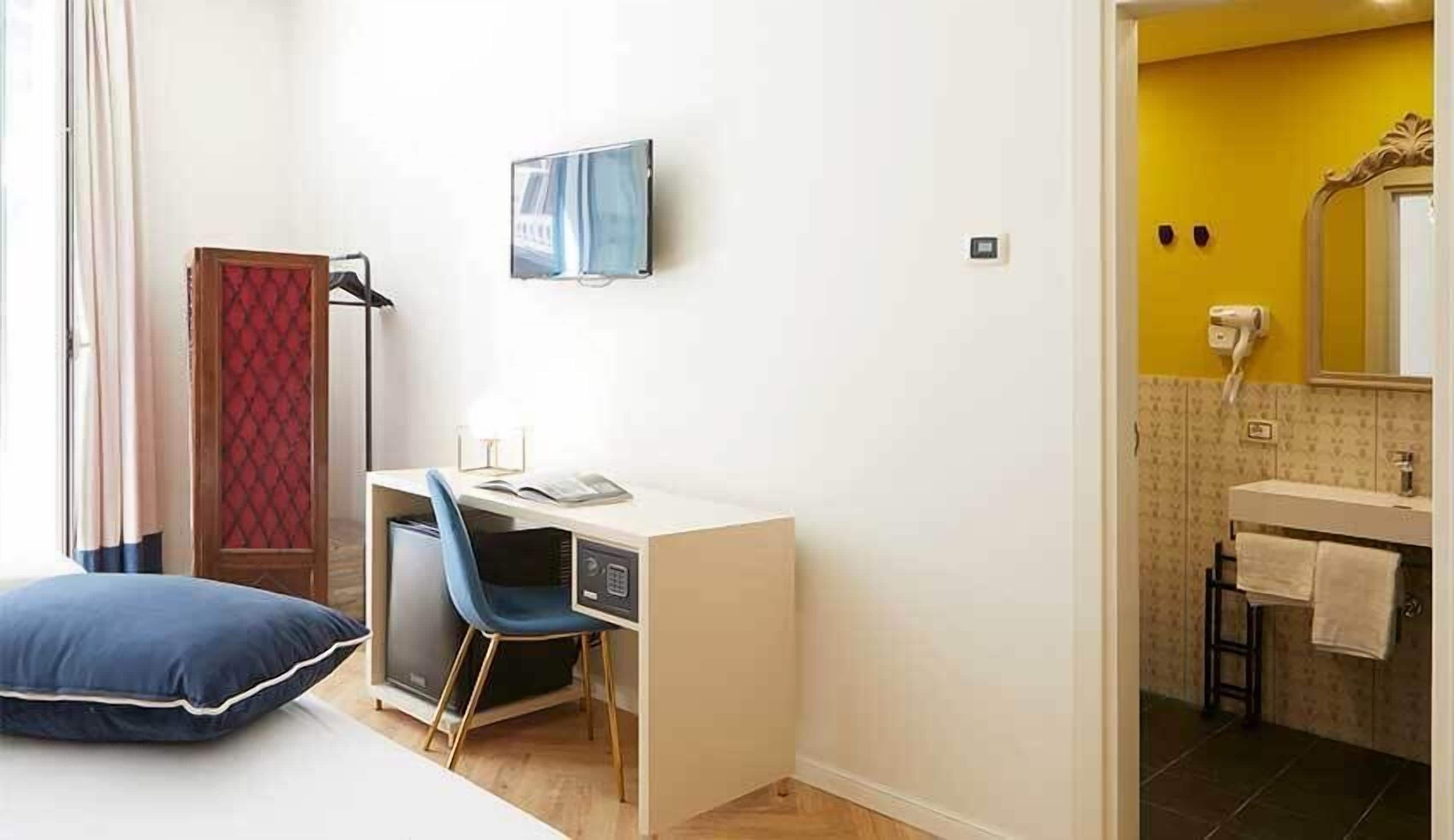 A hotel room with a bed, a desk with a chair, a TV, and a bathroom with a mirror and towel rack.