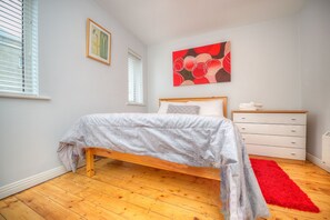 Un dormitorio con una cama de madera, un tapete rojo, un tocador blanco y un cuadro en la pared.