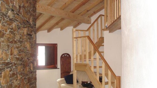 A room with a stone wall, a wooden staircase, a white chair, and a window.