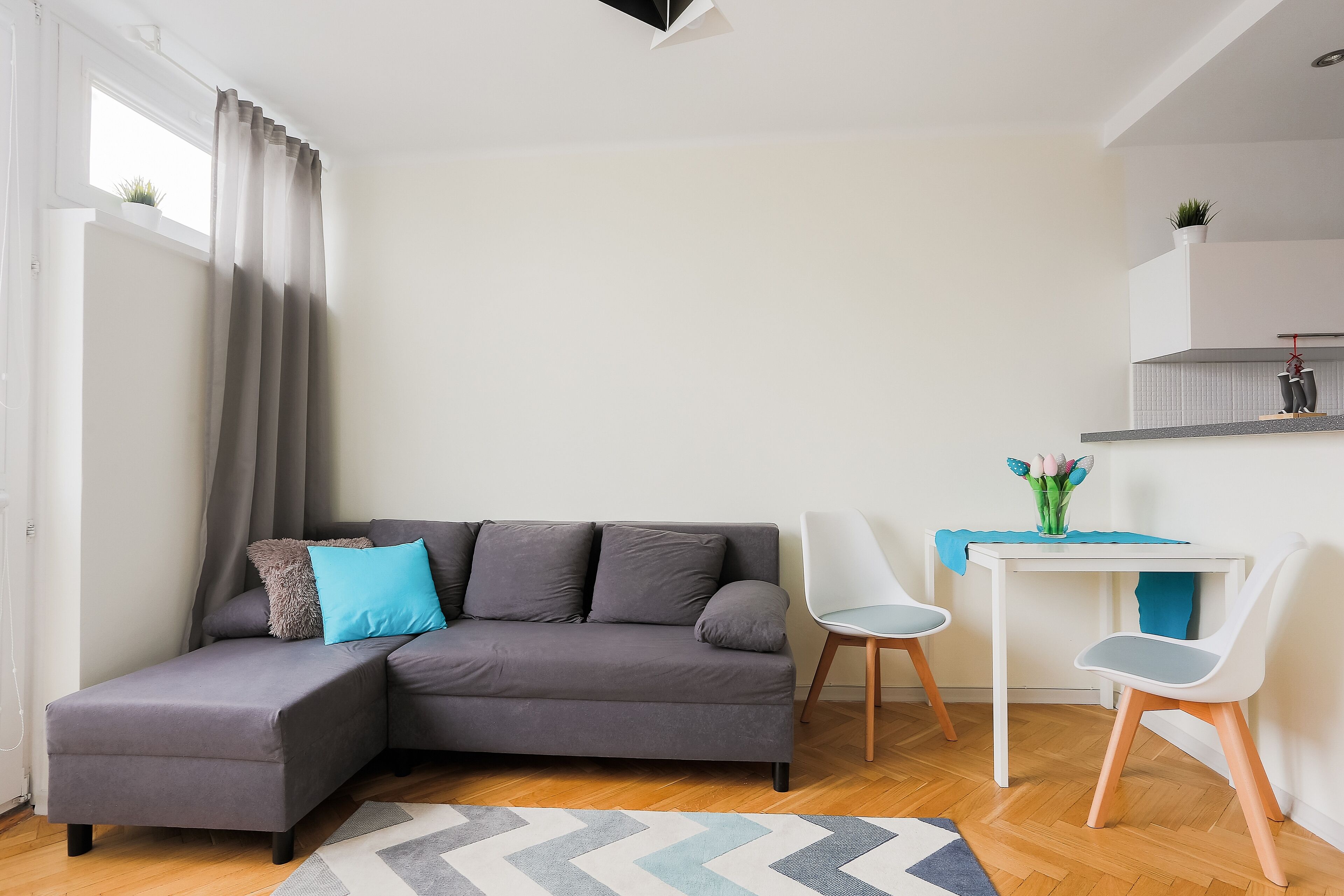 Una sala de estar moderna con un sofá seccional gris, un escritorio blanco y dos sillas blancas.